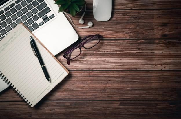 A tidy desk with a laptop, notebook, pen and reading glasses